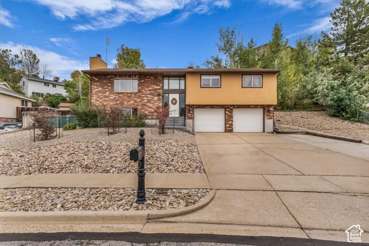 Split-level exterior featuring a brick and stucco facade, concrete driveway, two-car garage, and xeriscaped front yard
