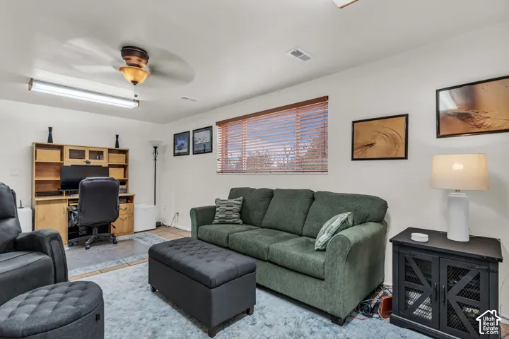 Living area featuring a built-in wooden desk unit, a multi-window frame with horizontal blinds, and a ceiling fan with integrated lighting