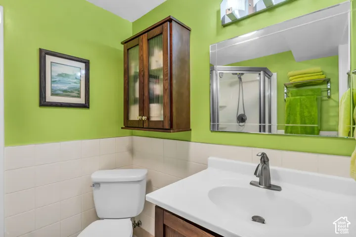 Bathroom featuring a vanity with a white countertop and integrated sink, a mounted wooden cabinet with glass-paneled doors, a rectangular frameless mirror, and a glass-enclosed shower stall