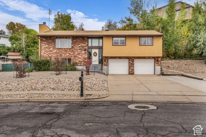 Split-level exterior featuring a brick and stucco facade, an attached two-car garage, and a concrete driveway