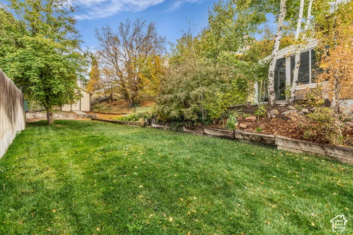 Backyard featuring a lawn, tiered timber retaining walls, mature trees, and a detached storage shed
