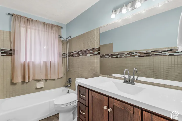 Bathroom featuring a vanity with dark wood-finish cabinetry, a white countertop, wall-to-wall mirror, tiled surround with a glass mosaic accent band, and a shower-tub combination