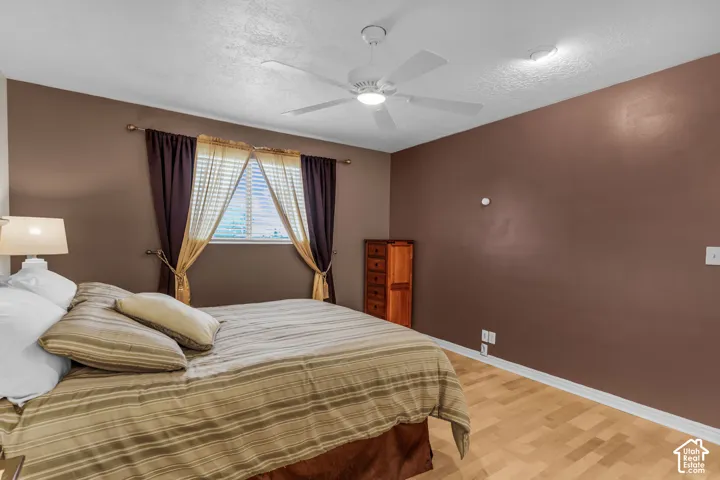 Room featuring wood-finish flooring, a white ceiling fan with integrated lighting, and a single window with a metal curtain rod