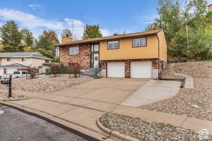Split-level exterior featuring a brick and stucco facade, an attached two-car garage, concrete driveway, and xeriscaped front yard