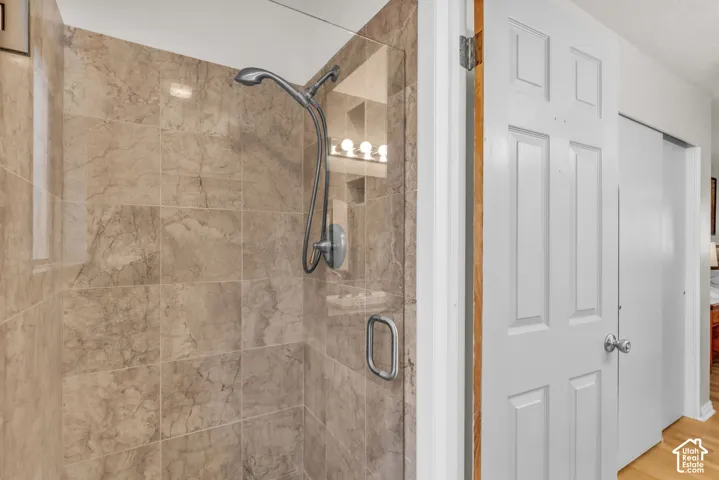Walk-in shower featuring large marble tile surround, frameless glass door, and adjustable-height handheld showerhead