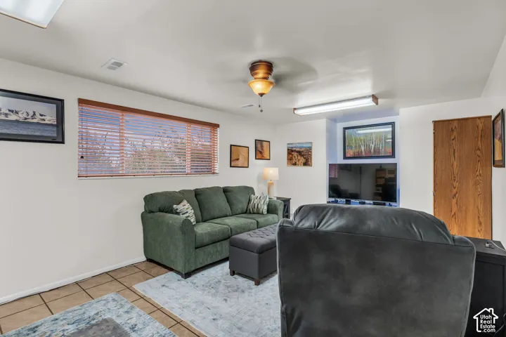 Neutral-toned interior space featuring ceramic tile flooring, horizontal window blinds, a central ceiling fan with an integrated light fixture, and a recessed wall niche