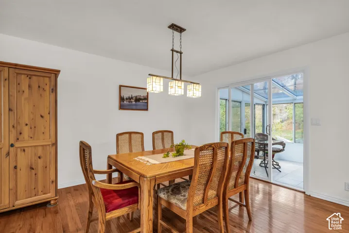 Dining area featuring oak wood flooring, a built-in cabinetry unit, a three-light linear pendant fixture with frosted glass shades, and sliding glass doors