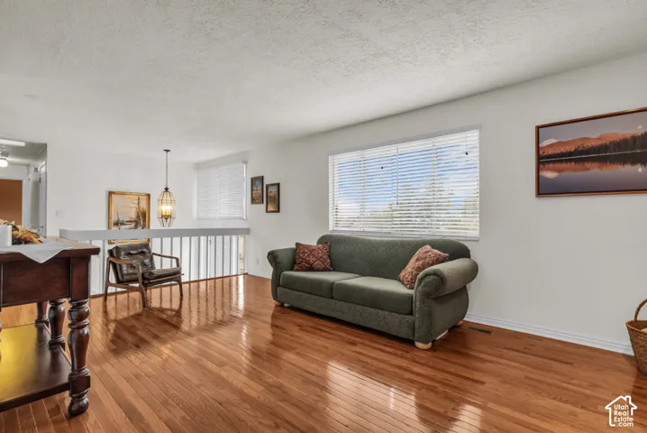 Wood-finish flooring, white walls, horizontal window blinds, and a decorative pendant light fixture