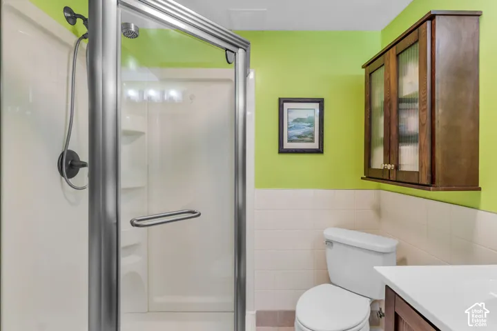 Corner shower stall with metallic frame, wall-mounted dark wood cabinetry, and white tile wainscoting