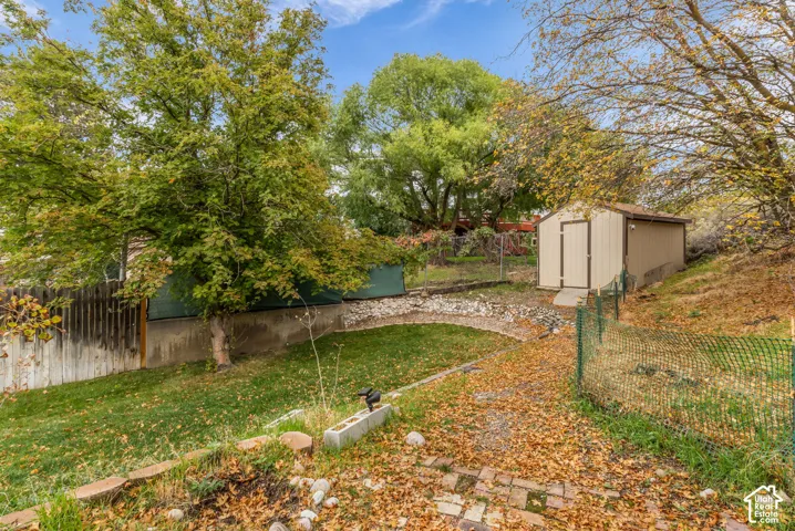 Backyard featuring a grass lawn, storage shed, wood and chain-link fencing, stone retaining wall, and brick paving
