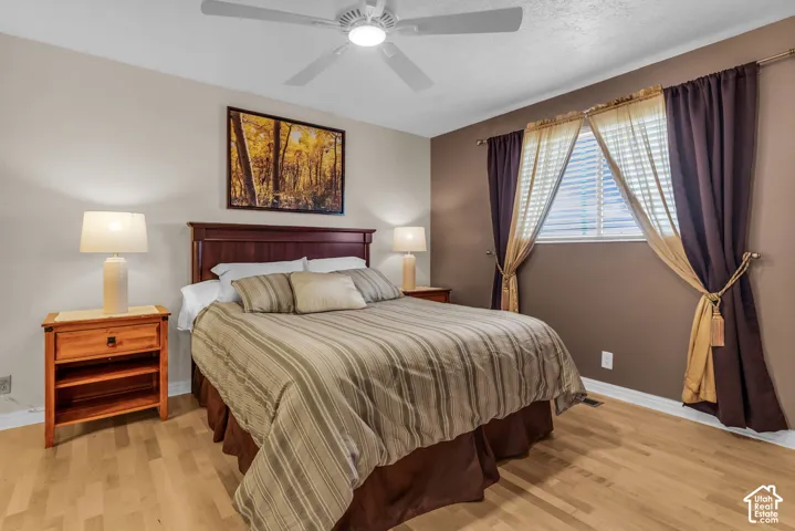 Bedroom featuring wood-finish flooring, a white ceiling fan with integrated lighting, and an accent wall