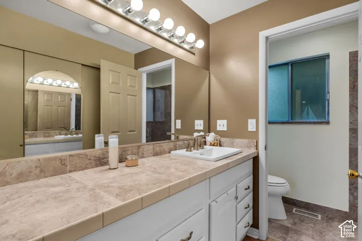 Bathroom vanity featuring a marble tile countertop, integrated white basin, white cabinetry, a large wall-mounted mirror, and an eight-bulb light fixture