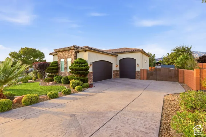 Stucco exterior featuring stacked stone accents, arched garage doors, a stamped concrete driveway, and an attached side-gate entry