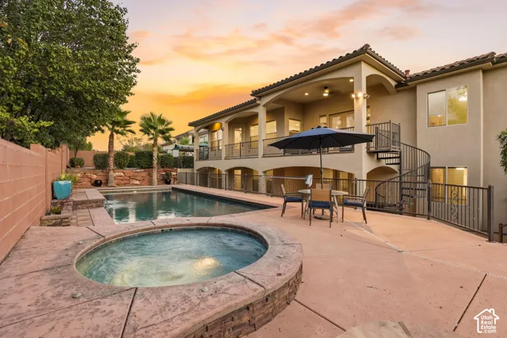 Multi-level exterior featuring a stone-clad spa, rectangular swimming pool, concrete patio, elevated balcony, and spiral staircase