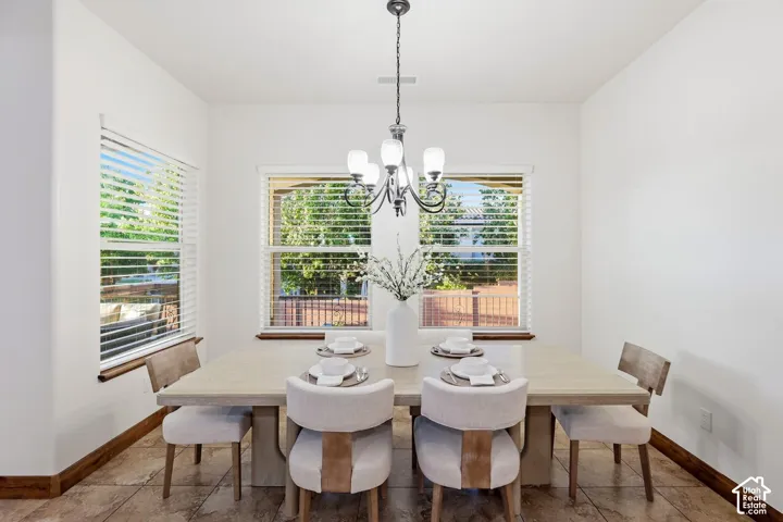 Dining area featuring tile flooring, three large windows with horizontal blinds, and a five-light metal chandelier