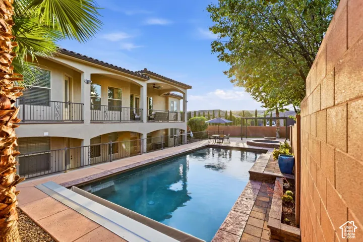 Two-story exterior featuring double-level covered balconies with wrought-iron railings, an in-ground swimming pool with an integrated spa, and decorative stone masonry hardscaping