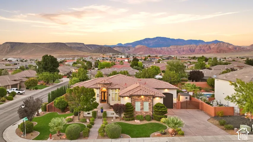 Single-story residence featuring a tile roof, stone masonry accents, a paved driveway, and manicured landscaping set against a mountain backdrop