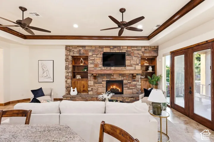 Floor-to-ceiling stone fireplace featuring a wood mantel and built-in shelving, complemented by crown molding, recessed lighting, dual ceiling fans, and French doors