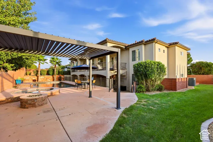 Rear exterior featuring a concrete patio with a metal pergola, a stone-surrounded hot tub, a swimming pool, and a spiral staircase