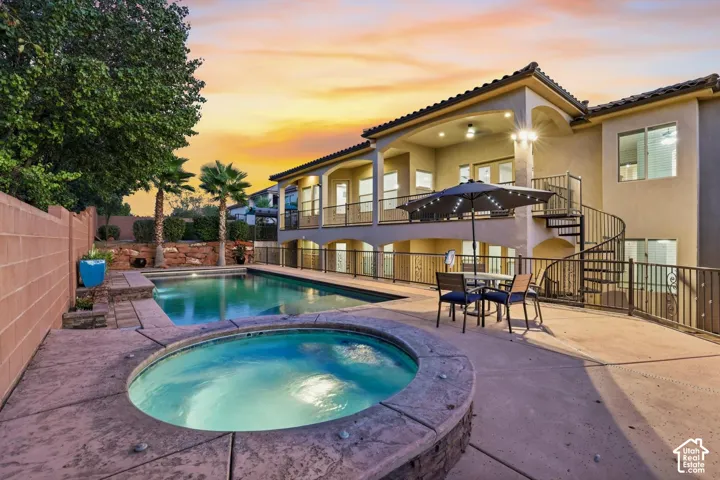 In-ground pool featuring a raised spa, expansive concrete decking, covered patio, and metal spiral staircase