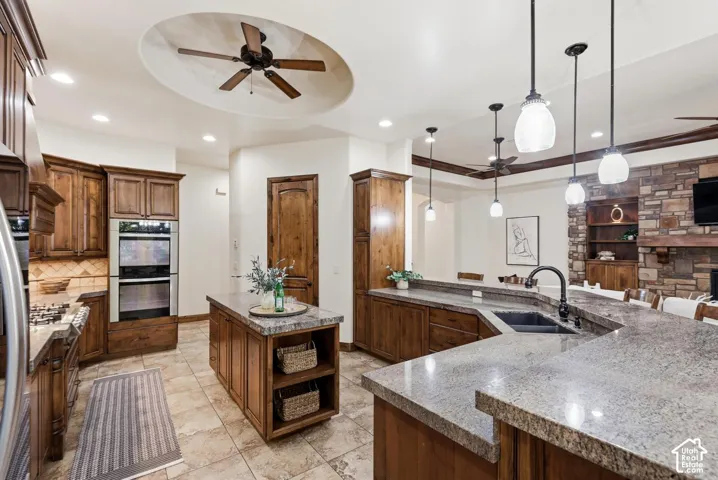Kitchen featuring custom wood cabinetry, stone-surface countertops, built-in double wall ovens, recessed circular ceiling detail with integrated fan, and pendant lighting