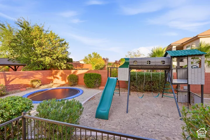 Private backyard enclosed by a masonry wall featuring an in-ground trampoline and a built-in play structure