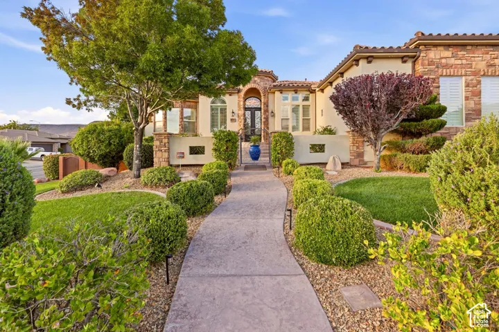 Stucco and stone veneer exterior featuring an arched entryway, decorative stucco wall accents, clay tile roofing, and a winding stamped concrete walkway