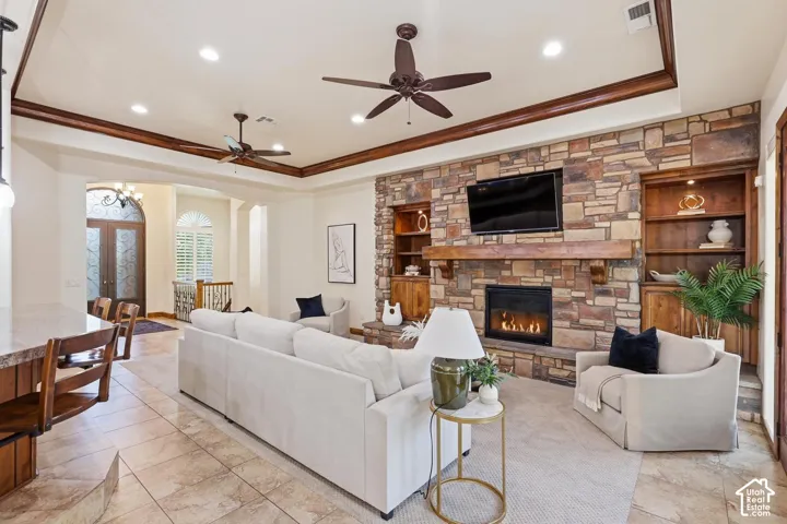 Stone-clad fireplace with a natural wood mantel, built-in wooden shelving, tray ceilings with crown molding, and recessed lighting