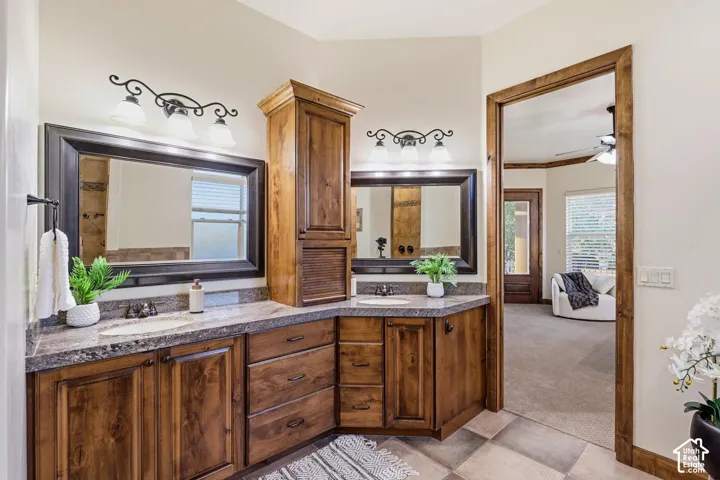 Bathroom featuring wood-finish cabinetry, stone-patterned countertops, dual framed vanity mirrors, and wall-mounted three-light fixtures