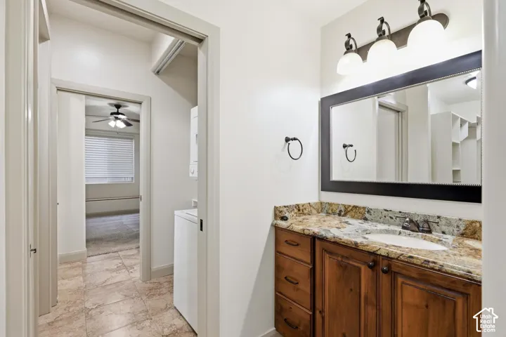 Vanity featuring a stone countertop, an oval under-mount sink, wood-finish cabinetry, a framed mirror, and three-bulb vanity lighting, finished with tile flooring
