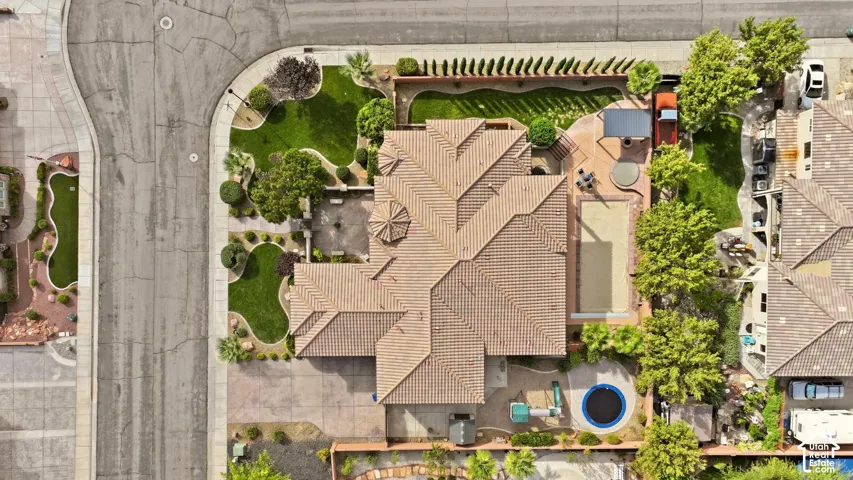 Corner lot residence featuring a tile roof, paved driveway, swimming pool, and professional landscaping with mature trees