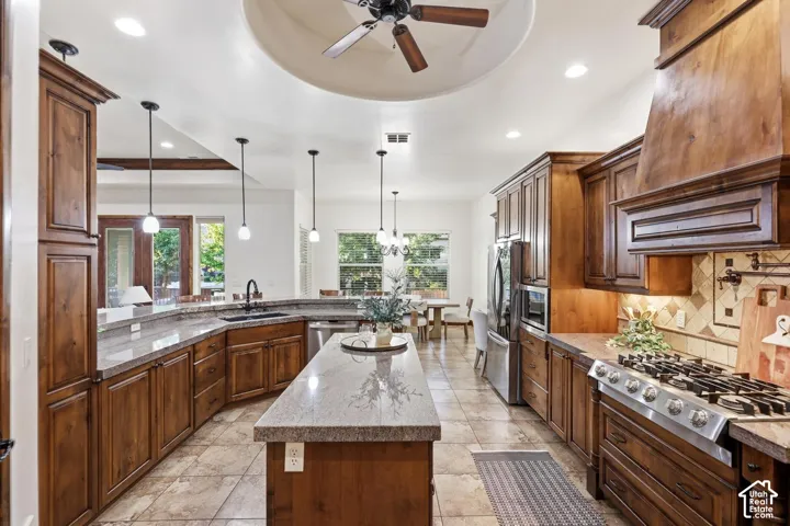 Kitchen featuring stained wood cabinetry, stone countertops, a large center island, stainless steel gas range with an integrated hood, and tile flooring