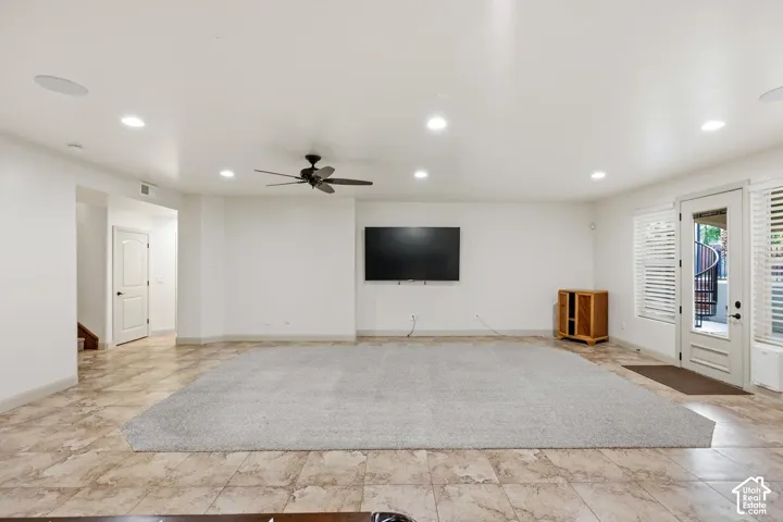 Spacious interior featuring recessed lighting, a ceiling fan, tiled flooring, integrated wall-mounted television, and a glass-paneled exterior door