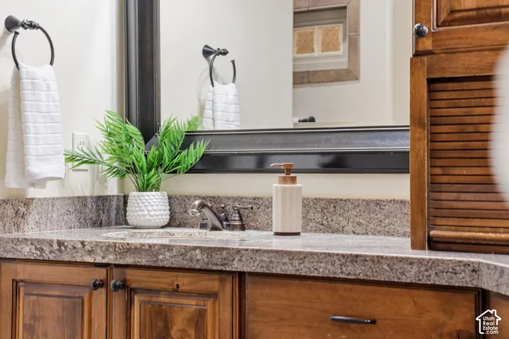 Bathroom vanity featuring raised-panel wood cabinetry, speckled stone countertop, integrated sink, metal widespread faucet, and large rectangular mirror with a dark wood frame