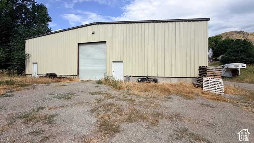 Metal-sided shop structure featuring a concrete foundation, one large roll-up bay door, two personnel access doors, and a gravel exterior surface