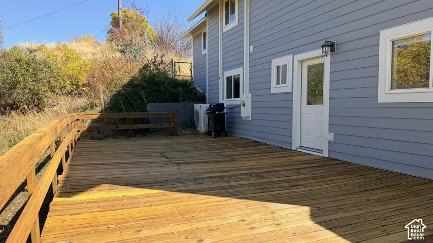 Spacious outdoor deck with natural wood railing, light blue horizontal siding, white trim windows, and a glass-paneled entry door