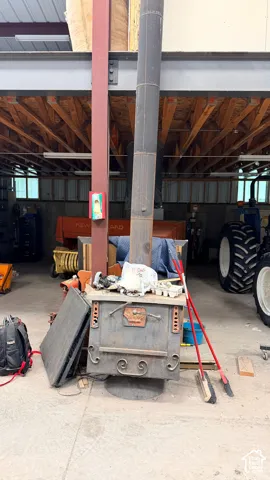 Freestanding metal wood-burning stove with vertical chimney flue, exposed timber-frame ceiling joists, steel support column, and concrete flooring
