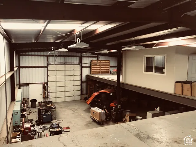 Large industrial space with high ceilings, an overhead door, and a built-in office structure with an exterior window