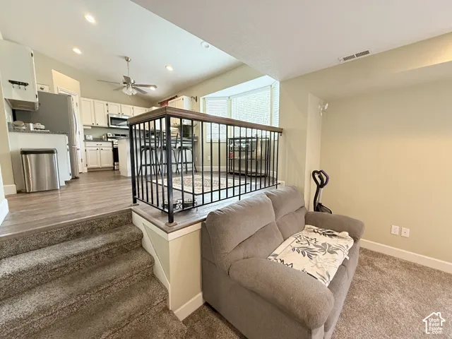Split-level interior featuring a raised kitchen area with wood-finish flooring, white cabinetry, integrated stainless steel appliances, and a metal railing with a wood cap