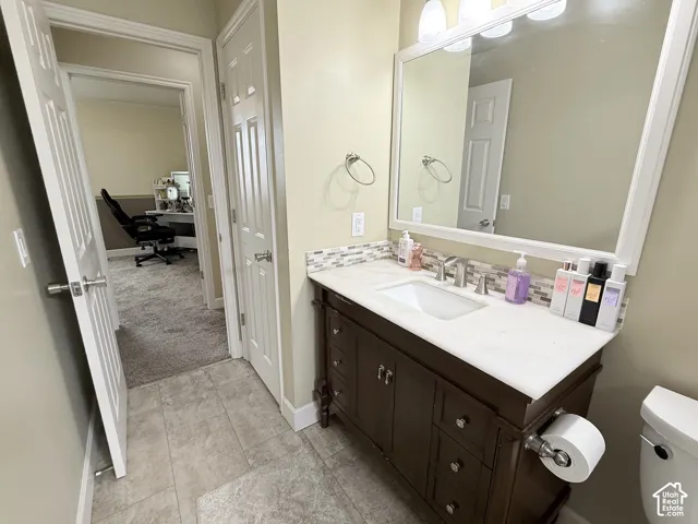Dark wood-finish vanity with stone-style countertop, rectangular undermount sink, multi-tone glass tile backsplash, and oversized vanity mirror with integrated lighting