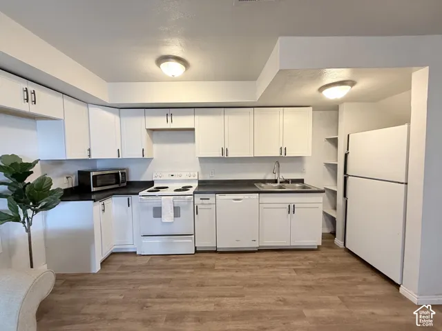 Kitchen featuring white shaker-style cabinetry, dark solid-surface countertops, built-in shelving, integrated dishwasher, and wood-finish flooring
