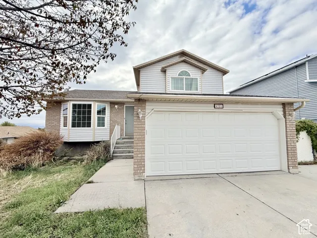 Split-level exterior featuring a brick facade, vinyl siding, attached two-car garage, bay window, and concrete driveway