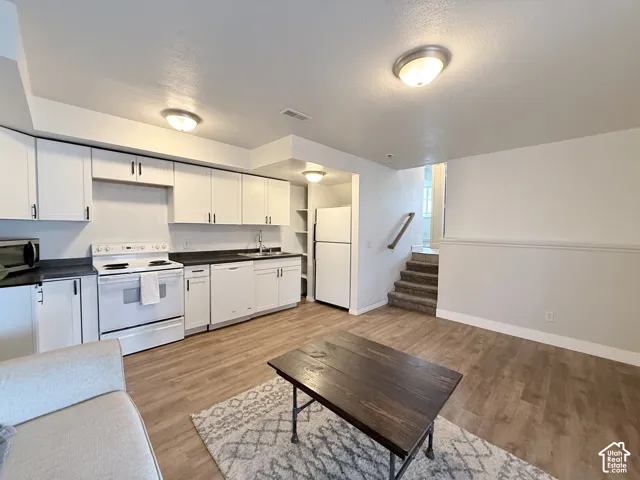 Kitchen featuring white shaker-style cabinetry, dark solid-surface countertops, wood-finish flooring, and recessed ceiling lighting