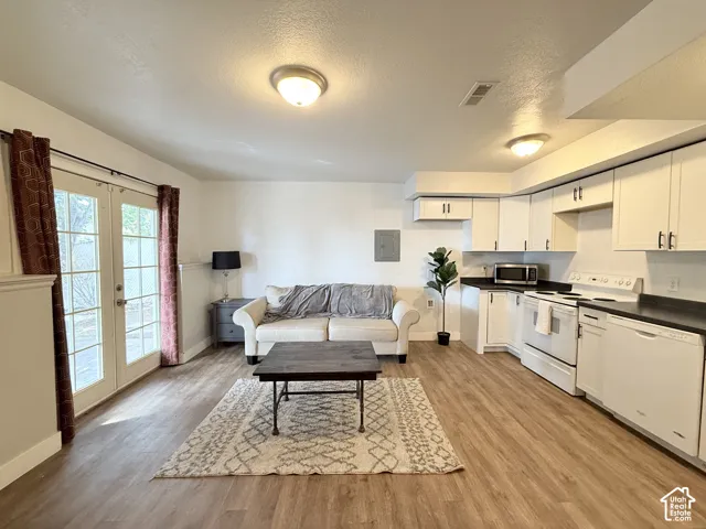Kitchen featuring white cabinetry, dark countertops, white appliance suite, wood-finish flooring, and dual-pane glass doors