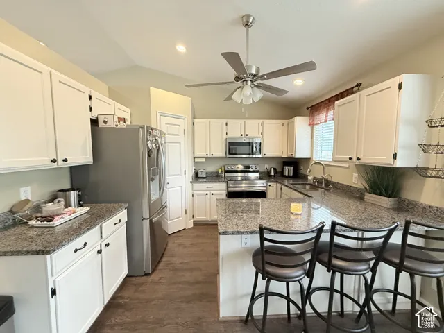 Kitchen featuring white cabinetry, stone-finish countertops, stainless steel appliances, breakfast bar, and wood-finish flooring