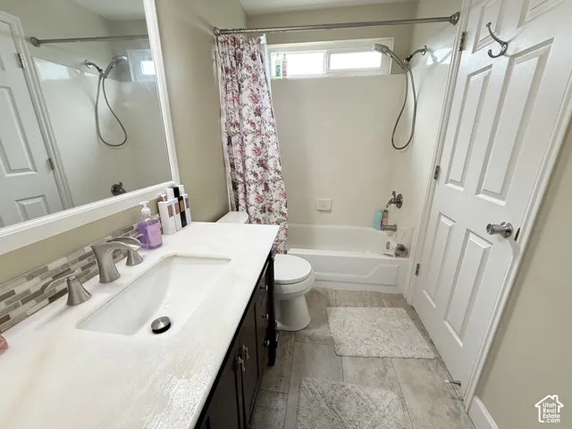 Bathroom featuring a dark-finish vanity with a rectangular undermount sink, light-toned countertop, mosaic tile backsplash, and a tub-shower combination with a handheld fixture