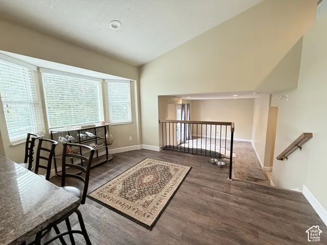 Vaulted ceilings, expansive bay window with integrated blinds, wood-finish flooring, and metal railing partition