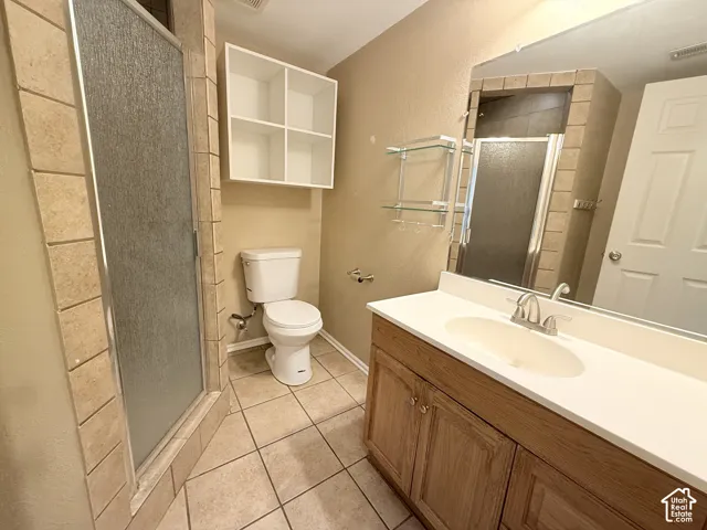 Bathroom featuring a vanity with a solid-surface countertop, tile flooring, walk-in shower with stone-tile surround, and built-in wall cabinetry