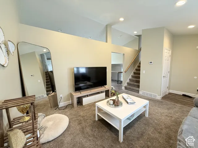 Vaulted ceilings with recessed lighting, carpeted flooring, and a staircase with a wooden handrail