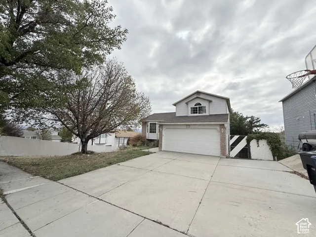Split-level exterior featuring light-toned horizontal siding, brick accents, an arched window, and an attached two-car garage with a concrete driveway